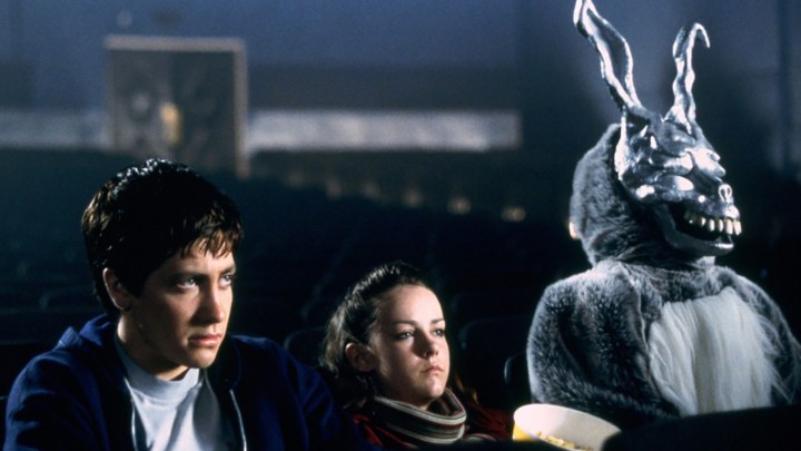 A young man, girl, and a man dressed as a rabbit sit in a movie theater in Donnie Darko.